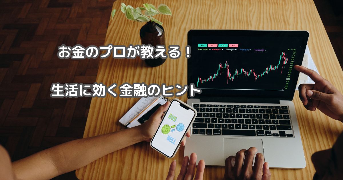 木製のテーブルに、株価チャートを表示したノートパソコンと、売買ボタンが表示されたスマートフォンが置かれている画像。